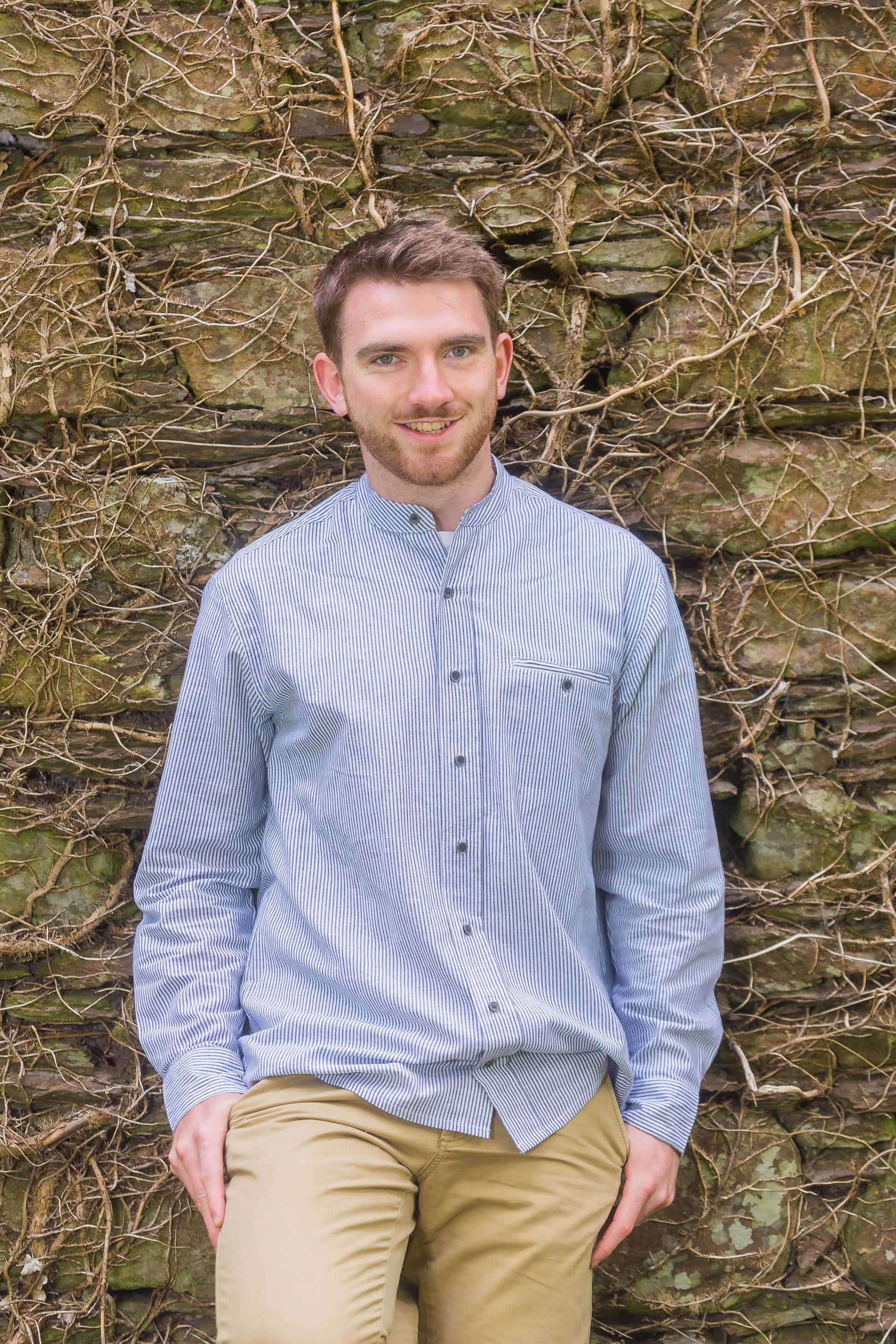 Blue and white striped linen shirt with a stand collar, sold in London, Ontario, shown on an Irish bloke leaning on a wall. Shirt is for men or women.