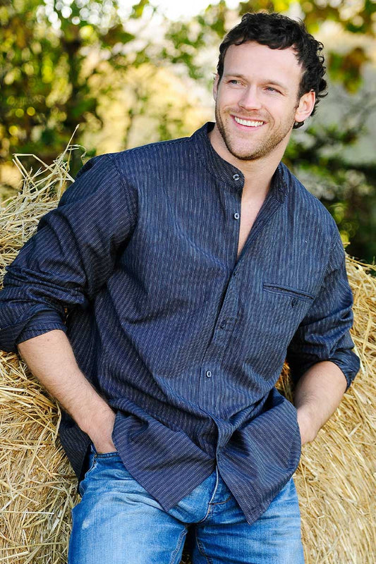 Blue and white striped linen shirt with a stand collar, sold in London, Ontario, shown on an Irish bloke leaning on straw. Shirt is for men or women.